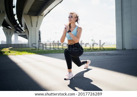 Motivating photo. Fitness figure a woman trains on the street in the city. A strong, confident athlete, a runner leads a healthy lifestyle. Exercises stretching muscles for fitness are active.