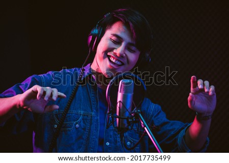 Asian male singer recording songs by using a studio microphone and pop shield on mic with passion in a music recording studio. Performance and show in the music business.