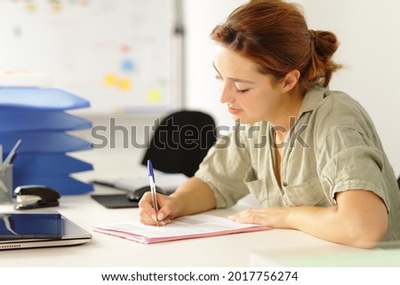 Relaxed woman working filling paper form on a desk at office