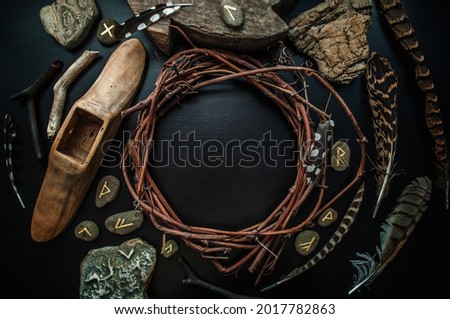 Rune stones, wreath, feathers and rocks on a black table. Future reading concept. Copy space. Royalty-Free Stock Photo #2017782863