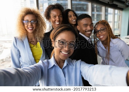 Smiling beautiful millennial african american business woman making selfie photo with motivated happy mixed race diverse colleagues partners, having fun entertaining together in modern workplace. Royalty-Free Stock Photo #2017793213