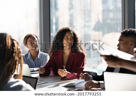 Concentrated young african american female leader boss negotiating business ideas or developing project growth ideas with motivated mixed race employees workers managers at brainstorming meeting. Royalty-Free Stock Photo #2017793255