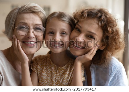 Head shot portrait happy three generations of women posing for family picture together, smiling mature grandmother and mother with adorable little girl looking at camera, warm family relationship