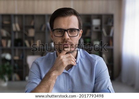 Thoughtful young man. Headshot portrait of concentrated bearded male teacher analyst look at camera think on idea. Pensive millennial businessman in glasses listen to partner communicate by video call