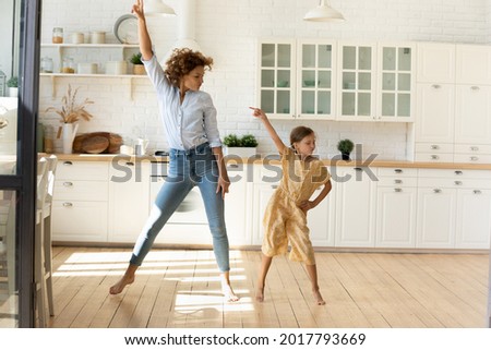 Happy mother and little daughter moving to favorite music in modern kitchen together, young mom teaching adorable kid girl to dance, family engaged in funny activity at home, enjoying leisure time Royalty-Free Stock Photo #2017793669
