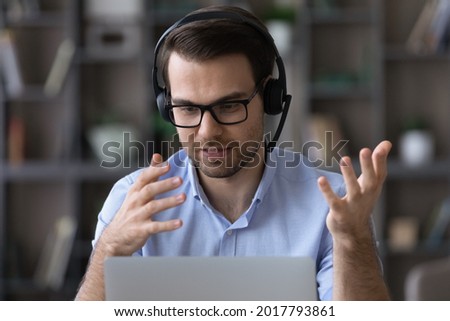 Virtual helpdesk. Young man in eyewear and wireless headset call center agent give technical support to customer. Male telemarketer speak by video call look on pc screen offer goods service to client Royalty-Free Stock Photo #2017793861