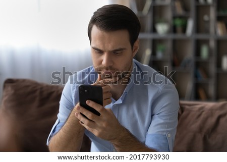 Need to think. Thoughtful millennial man sit on couch rub chin read serious important message on phone screen. Concentrated pensive young businessman receive unexpected news ponder on problem solution Royalty-Free Stock Photo #2017793930