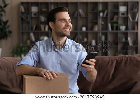 Satisfied millennial man sit on couch hold postal parcel smartphone enjoy express delivery courier service ordered by phone call. Happy young male client give positive feedback to package tracking app Royalty-Free Stock Photo #2017793945