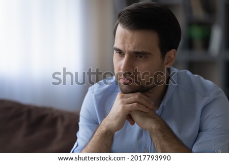 Having troubles. Sad upset young man sit on sofa put chin on folded hands lost in bad thoughts ponder on life business love problems. Depressed casual guy grieve alone overcome heartbreak. Copy space Royalty-Free Stock Photo #2017793990