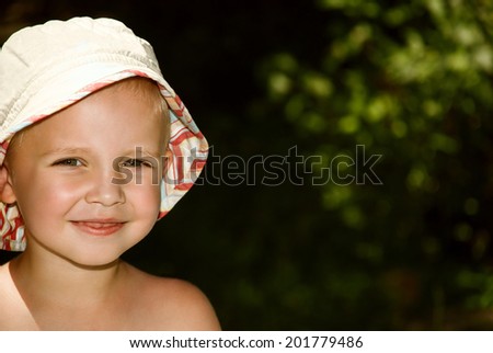 Portrait of little boy in a panama hat on background of green foliage in sunny weather.