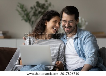 Happy millennial couple enjoying dating at home, watching and discussing movie on laptop, relaxing on couch, talking, laughing. Husband and wife making paying bills, paying mortgage, insurance fees Royalty-Free Stock Photo #2017806710