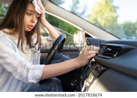 Girl driver has problem with a non-working conditioner, hand checking flow cold air, being hot during heat wave in car, suffering from summer hot weather, wipes sweat from her forehead with tissue.  Royalty-Free Stock Photo #2017818674