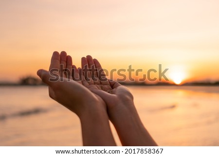 Woman hands place together like praying from nature in front of sunset beach background.