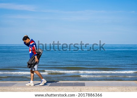 Man teennager wearing sportwear and shoes playing,walking and holding surf skate on the road oudoor in the morning. Relax and enjoy extreme surfskate on summer holiday at the beach.