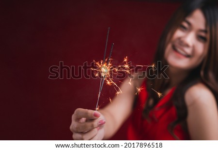 Young woman is happily in red dress celebrating the new year holding fireworks.