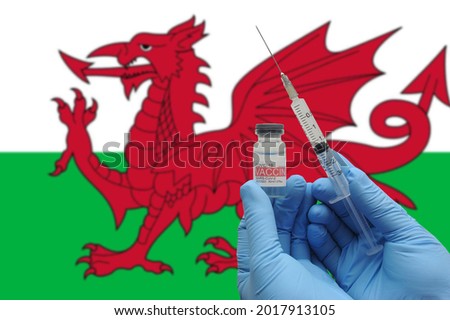 COVID-19 vaccine. Hands in blue medical gloves holding a vaccine bottle and syringe with Wales flag with blurred effect background
