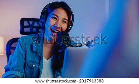 Happy asia girl host record podcast use microphone wear headphone with laptop interview guest conversation for content in her home studio at night. Sound equipment concept. Content creator concept.