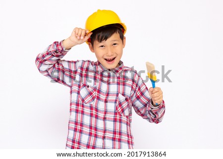 Little kid as a construction worker wearing yellow helmet with a paintbrush in his hand..White background studio picture.