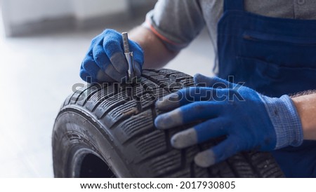 Mechanic checking tire tread depth and wear using a tire gauge, car maintenance concept Royalty-Free Stock Photo #2017930805