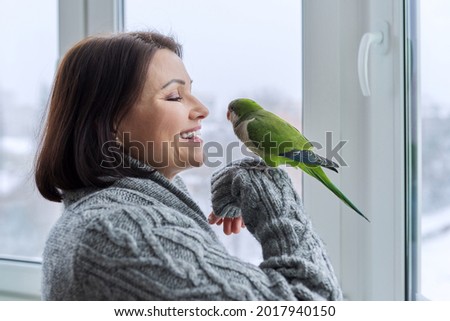 Middle aged woman and parrot together, female bird owner talking looking at green quaker pet Royalty-Free Stock Photo #2017940150