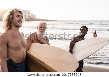 Diverse surfer friends holding surf boards after extreme water sport session with beach on background - Focsus on african man face