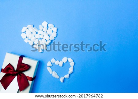 Red bow gift box decorated with heart-shaped stones on blue background.