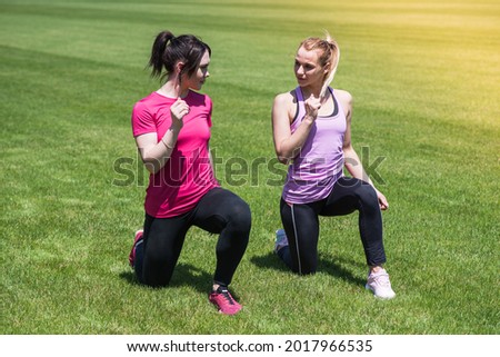Two women doing lunges in a studio on the grass