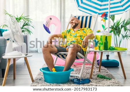 Man relaxing on a deckchair at home in the living room, he is having a staycation and pretending he is on a beach