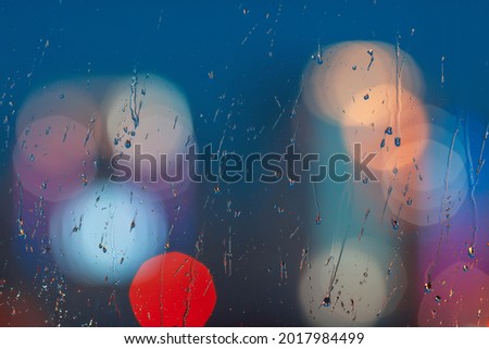 Raindrops on the surface of the window against the background of beautifully blurred city lights. High quality abstract blurry background