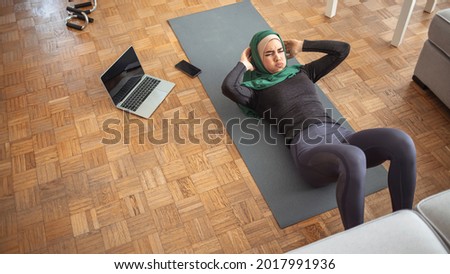 Sporty Muslim Lady In Hijab Doing Pilates Workout With Laptop At Home, Practicing Online Yoga, Religious Woman Training In Living Room During Quarantine, Enjoying Healthy Lifestyle, Copy Space