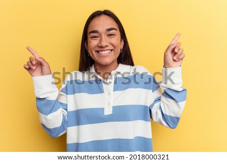 Young mixed race woman isolated on yellow background pointing to different copy spaces, choosing one of them, showing with finger.