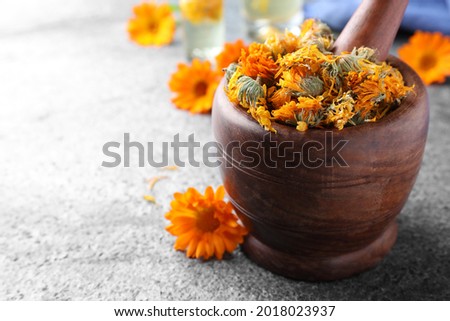 Wooden mortar with dry calendula flowers on light grey table, closeup. Space for text