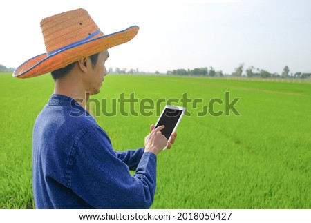 A male farmer wearing traditional clothes is using a smart tablet in a green field.