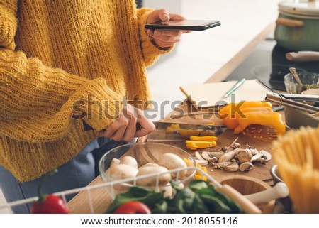 Young woman taking photo of sliced pepper in kitchen