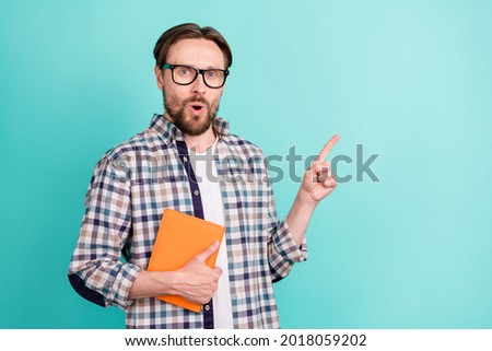 Photo of young man amazed shocked hold book point finger empty space ads choose isolated over teal color background