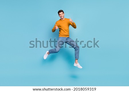 Photo of funky cute young man wear yellow sweater smiling jumping high showing thumbs up isolated blue color background Royalty-Free Stock Photo #2018059319