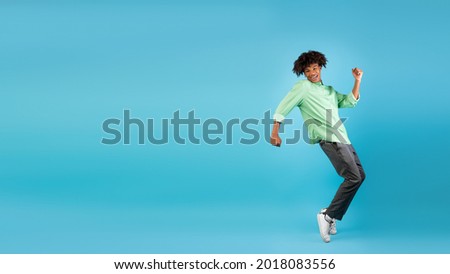 Excited african american teen guy fooling, standing on sneakers tiptoes, dancing and having fun over blue background, panorama with free space, studio shot