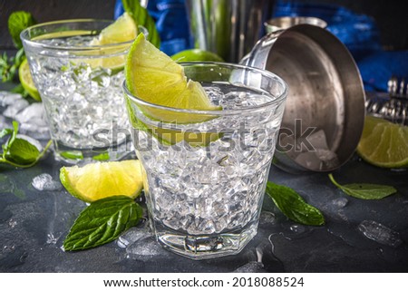 Summer paloma cocktail, vodka lime, mojito or gin tonic with lime wedge and crushed ice in rocks, two cold alcohol beverage glasses on black background copy space
