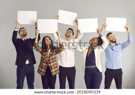 Group of five happy smiling people, office workers or friends, standing on gray background, holding white sheets of paper, empty signs, mockup banners, expressing opinion or giving positive feedback