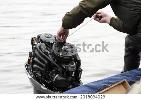 Boater hand start an outboard boat motor without the hood cap on the transom of the boat, emergency engine start with rope when broken starter or battery Royalty-Free Stock Photo #2018094029