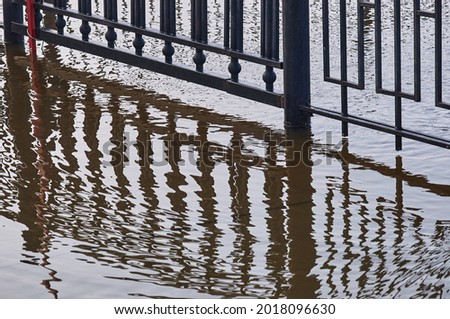A metal fence of a flooded embankment with reflections. Selective focus on the geometric grid. Distortion on the surface of the water.
