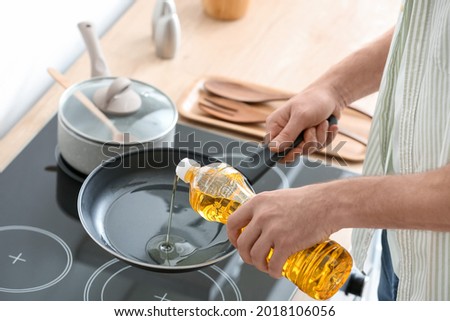 Man pouring sunflower oil on frying pan in kitchen Royalty-Free Stock Photo #2018106056