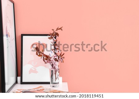 Vase with blossoming branches and pictures on shelf near color wall