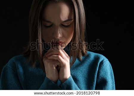 Religious young woman praying on dark background, closeup