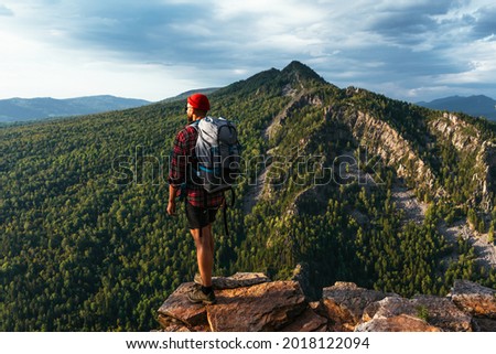 A traveler with a backpack in the mountains at sunset. Hiking in the mountains. Travel to Bashkiria, Russia. A man with a backpack on the background of the mountains, a rear view. Backpacking trips Royalty-Free Stock Photo #2018122094