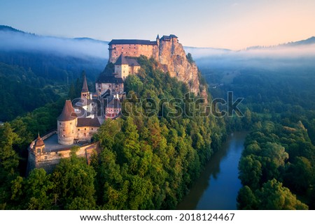 Panoramic, aerial view of Orava Castle, fantasy castle situated on a high rock above river, illuminated by rising sun, surrounded by deep forest and  mountains. Traveling concept background. Slovakia. Royalty-Free Stock Photo #2018124467