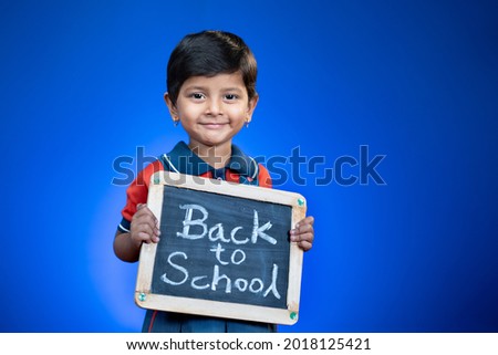 Happy smiling Indian school kid holding back to school sign board on blue backgrounds