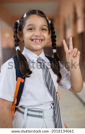 Portrait of school girl and showing v sign gesture with her hand.