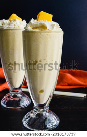 Mango Coconut Milkshakes Served in Fountain Glasses: Blended frozen drinks made with mango and coconut milk and topped with whipped cream