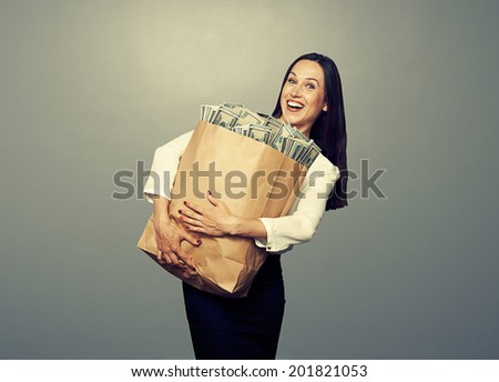 excited businesswoman holding paper bag with money and smiling. photo in studio over grey background